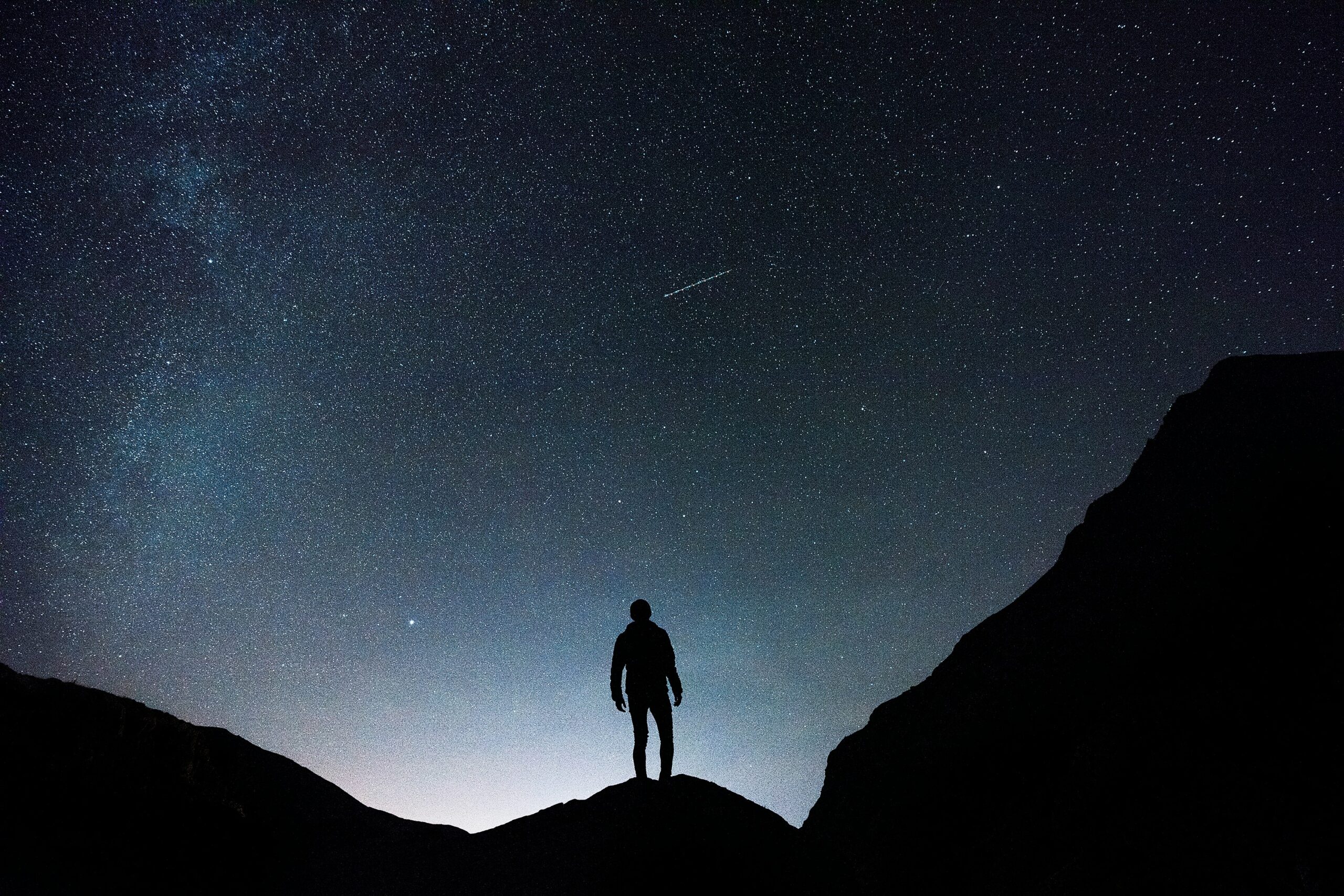 Silhouette of a person standing on hills with a stary sky.